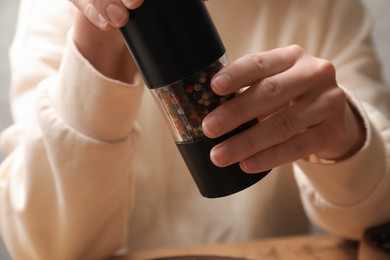 Photo of Woman grinding pepper with shaker at table, closeup