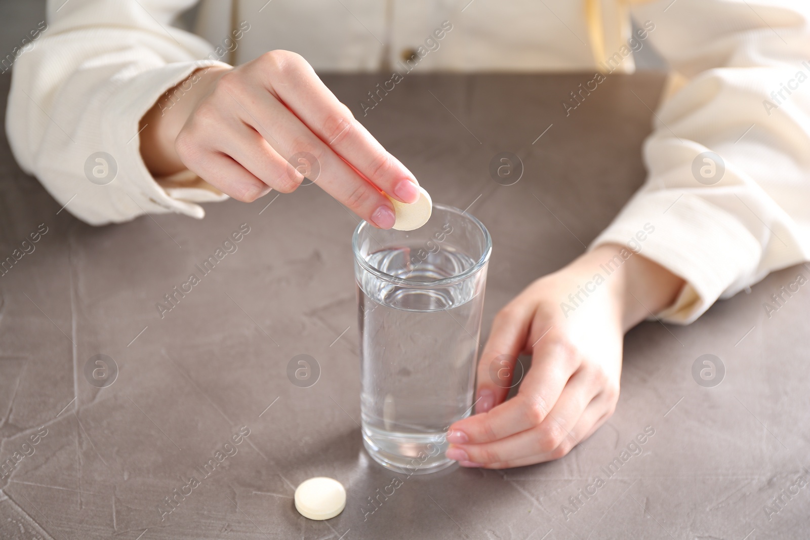 Photo of Woman putting effervescent pill into glass of water at grey table, closeup