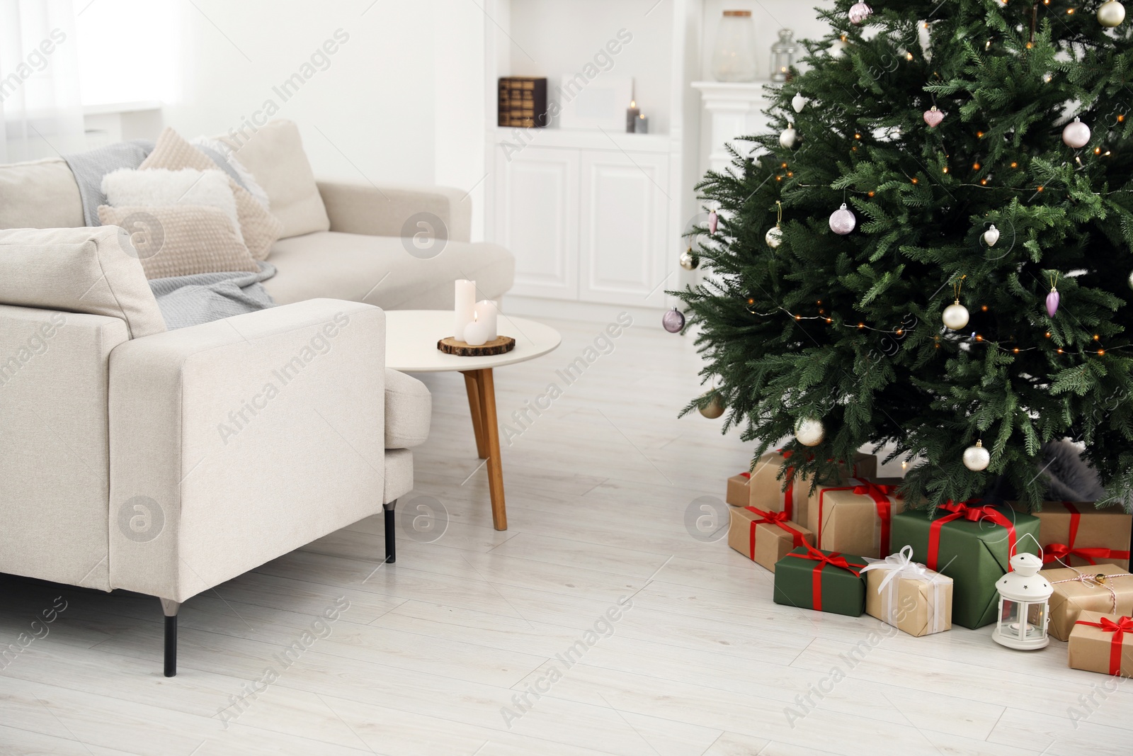 Photo of Beautifully wrapped gift boxes and lantern under Christmas tree in living room