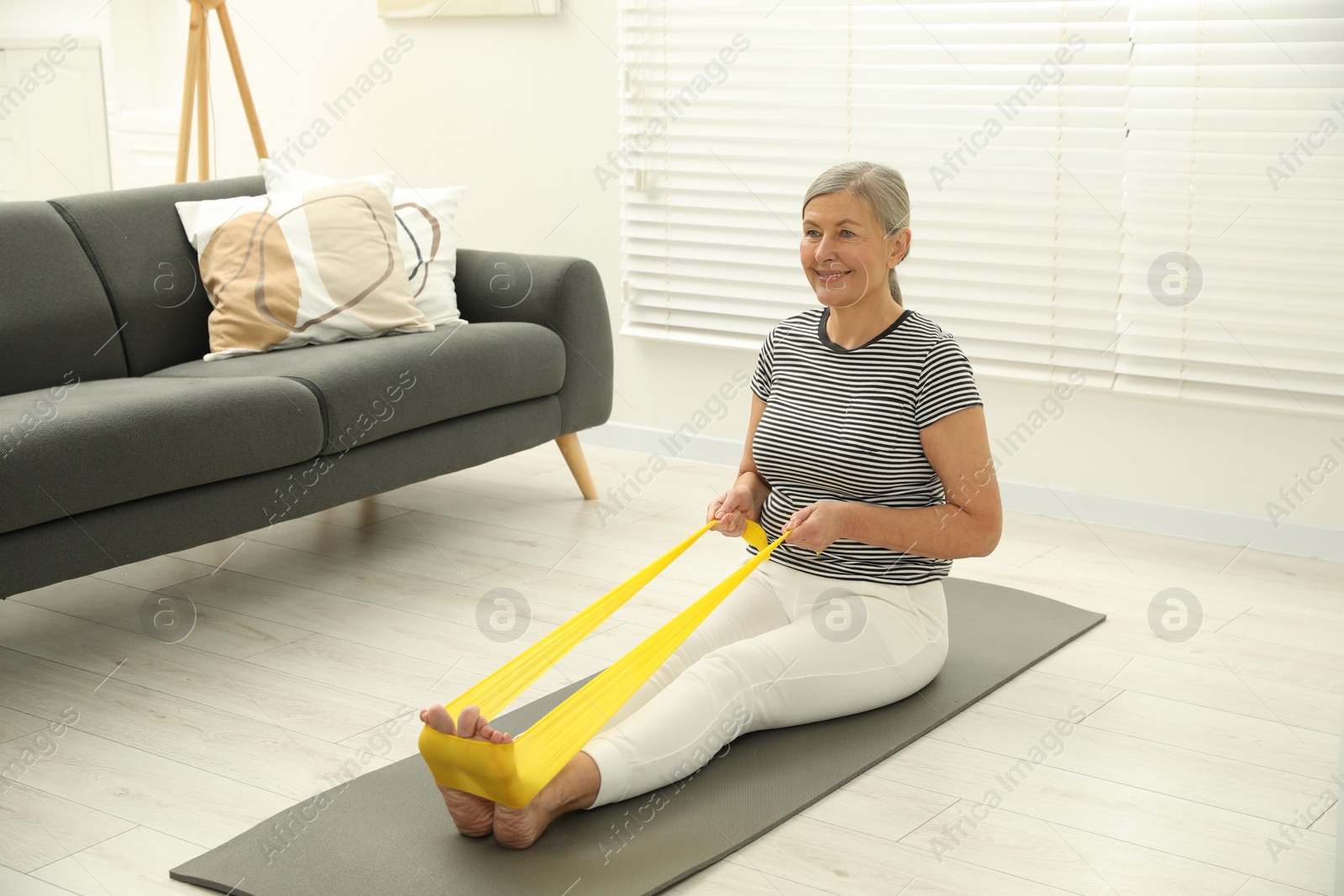 Photo of Senior woman doing exercise with fitness elastic band on mat at home