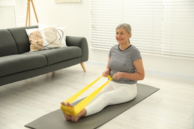 Photo of Senior woman doing exercise with fitness elastic band on mat at home