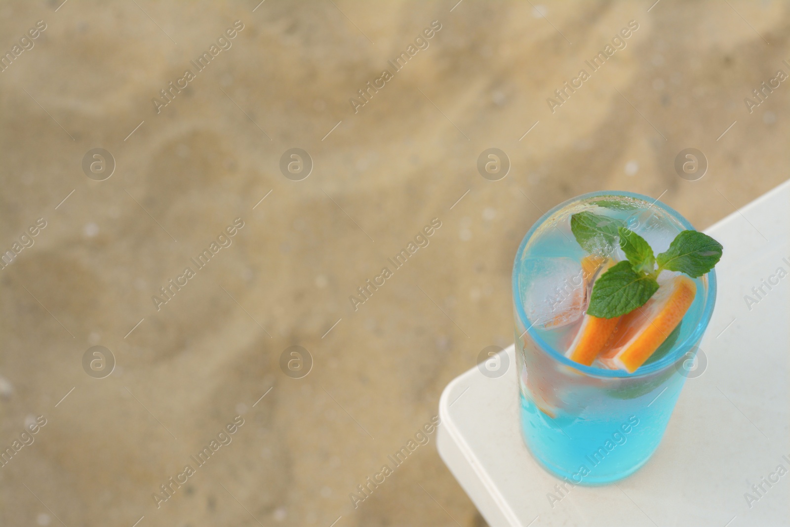 Photo of Glass of refreshing drink with grapefruit and mint on white table at beach, above view. Space for text