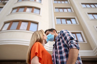 Photo of Couple in medical masks trying to kiss outdoors, low angle view