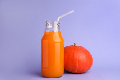 Photo of Tasty pumpkin juice in glass bottle and whole pumpkin on lavender color background