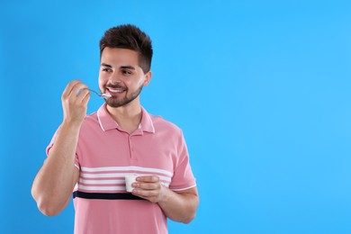 Photo of Happy young man eating tasty yogurt on light blue background. Space for text