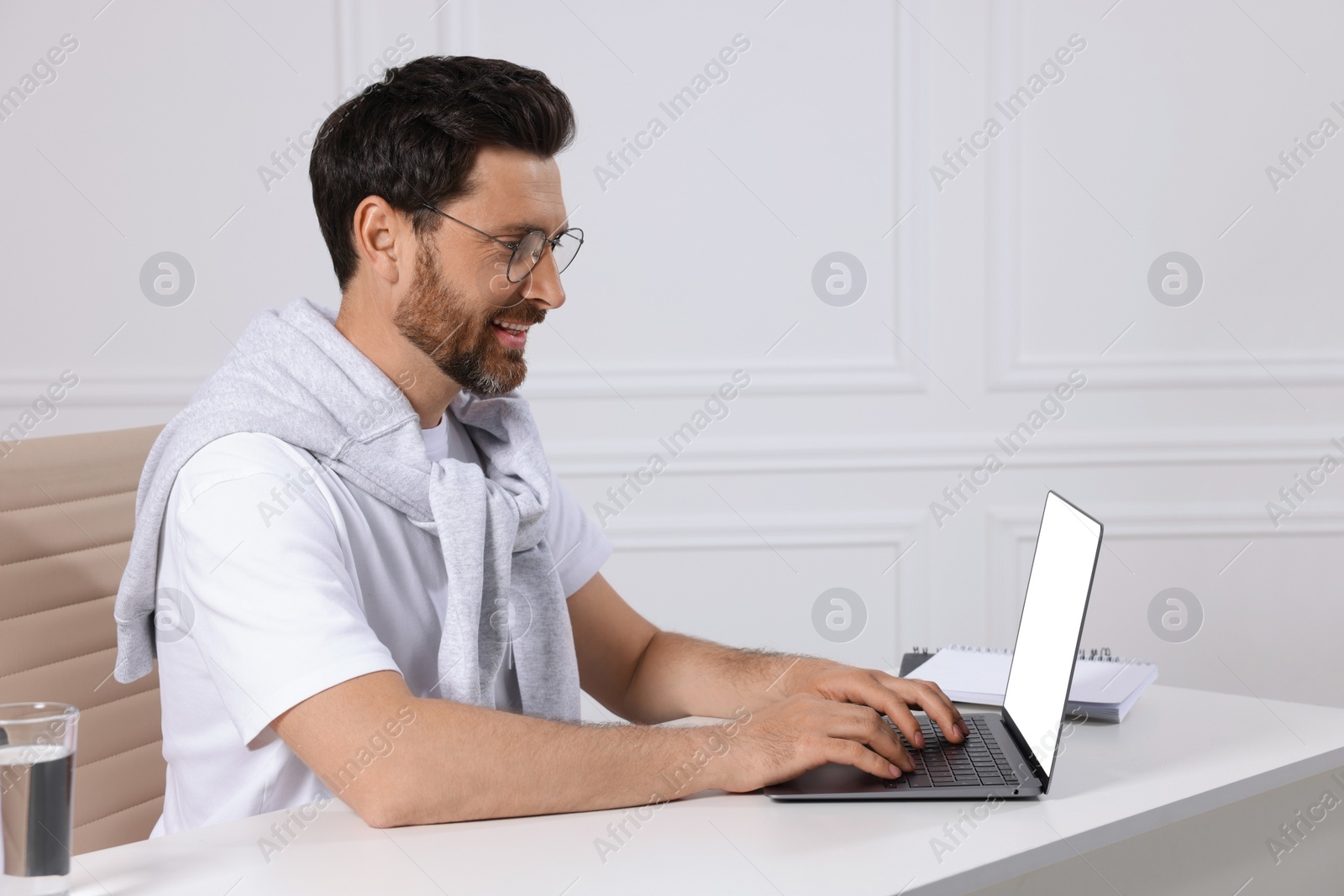 Photo of Man using laptop at white table indoors