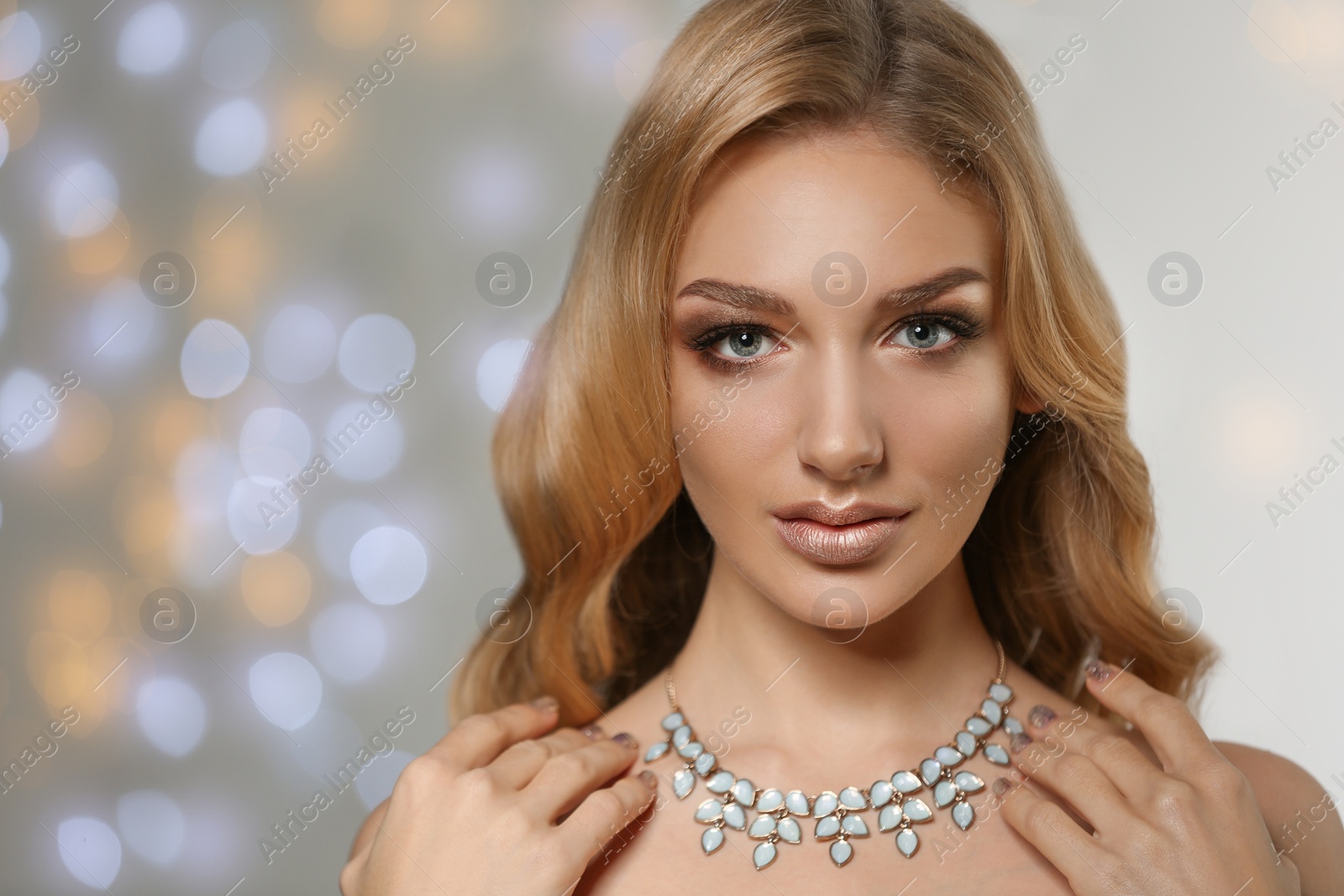 Photo of Beautiful young woman with elegant jewelry against defocused lights. Space for text