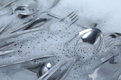 Washing silver spoons, forks and knives in foam, closeup