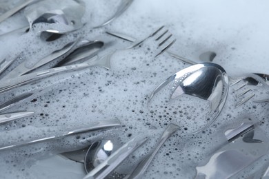 Photo of Washing silver spoons, forks and knives in foam, closeup