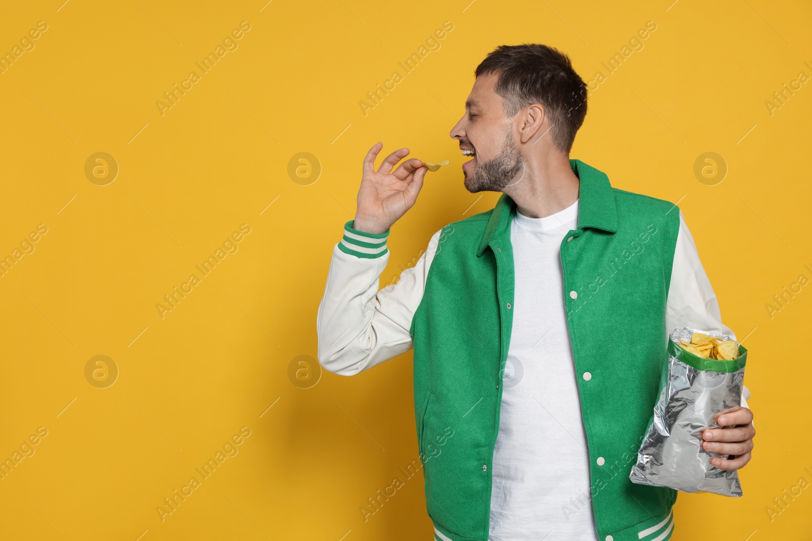 Photo of Handsome man eating potato chips on orange background, space for text