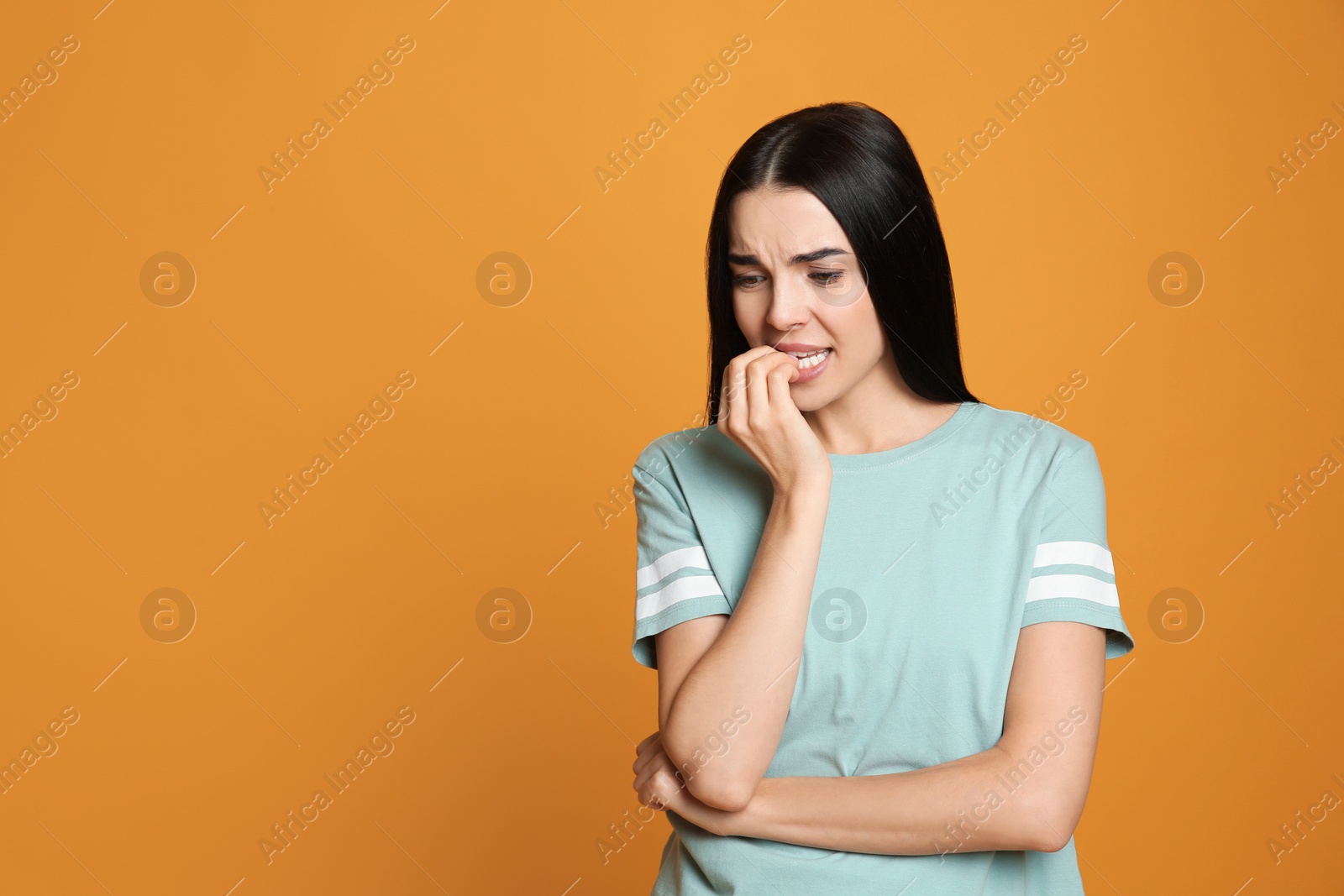 Photo of Young woman biting her nails on yellow background. Space for text