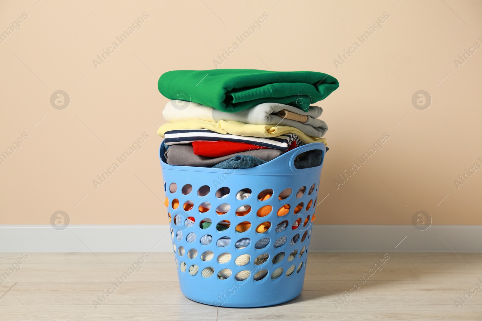 Photo of Plastic laundry basket with clean clothes on floor near beige wall