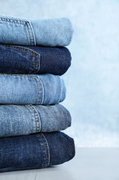 Stack of different jeans on light table against blue background