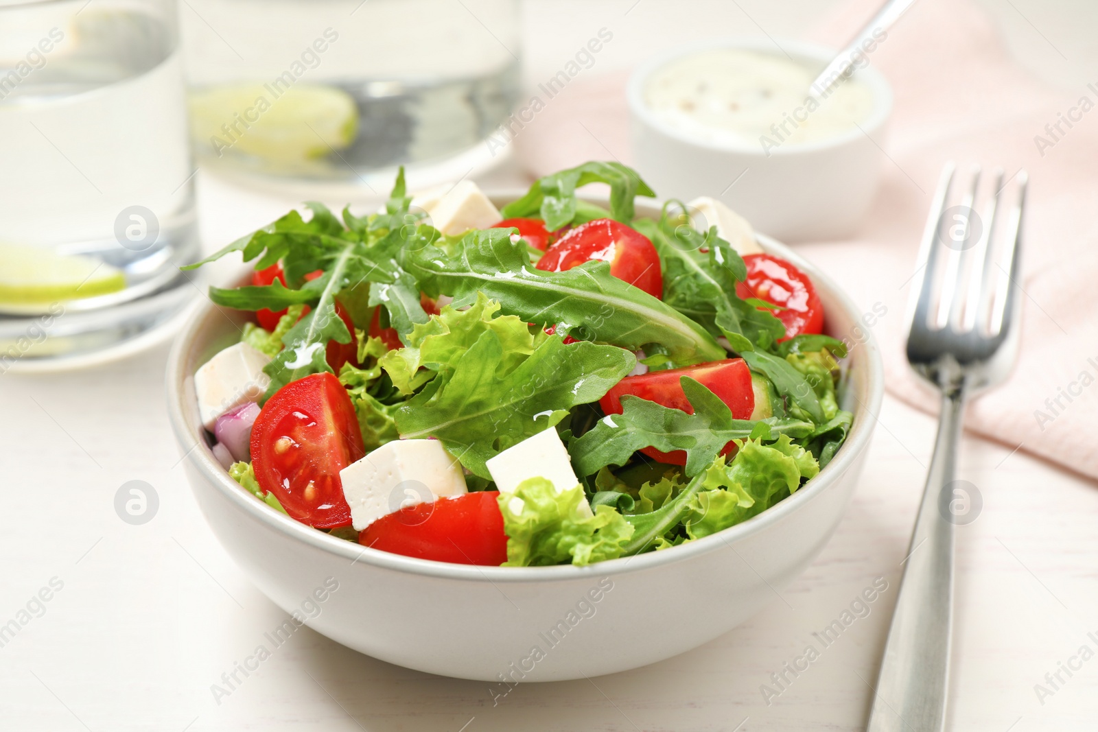 Photo of Delicious salad with arugula and vegetables on white table, closeup