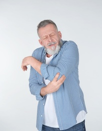 Man suffering from elbow pain on light background