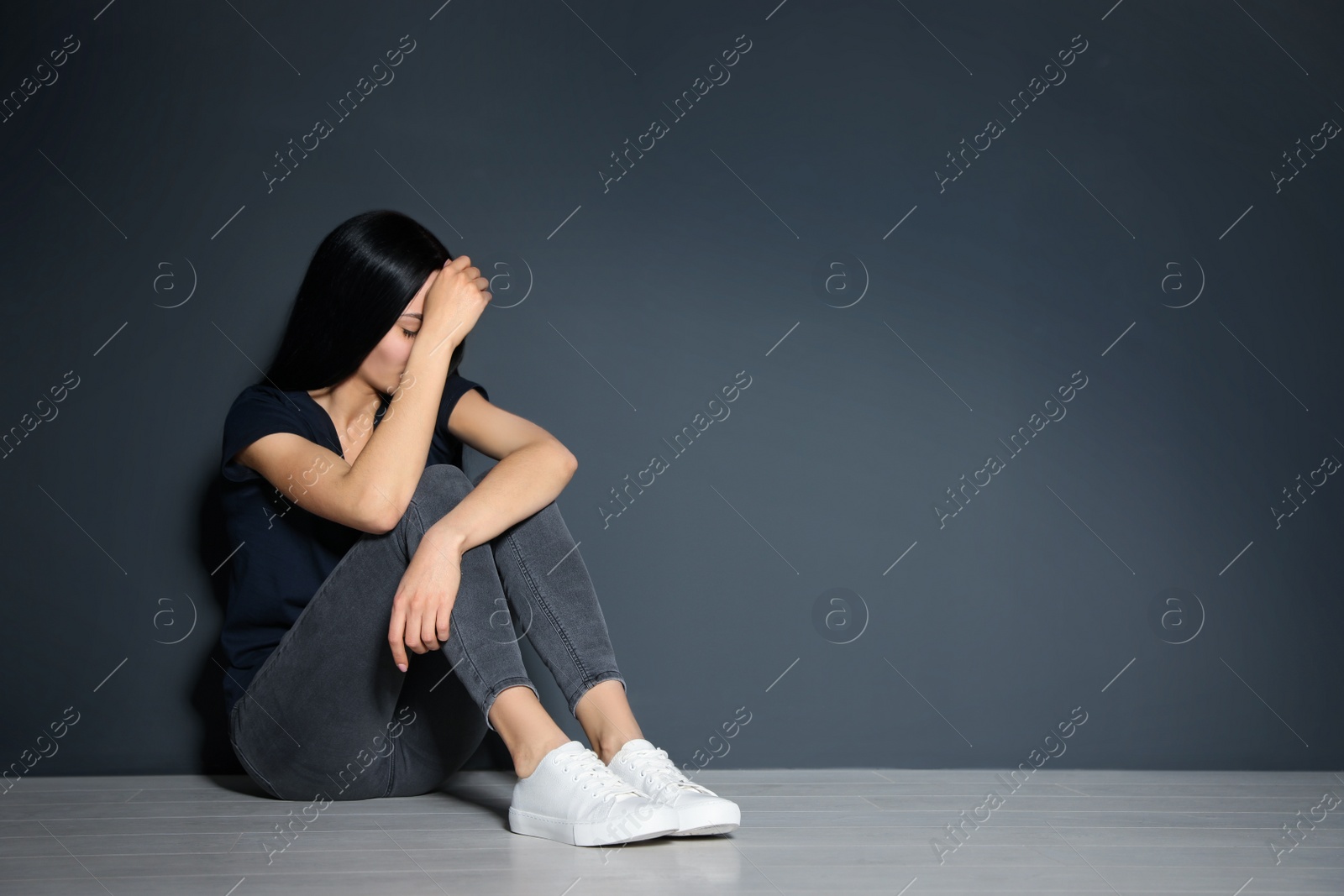 Photo of Upset young woman sitting on floor near grey wall. Space for text