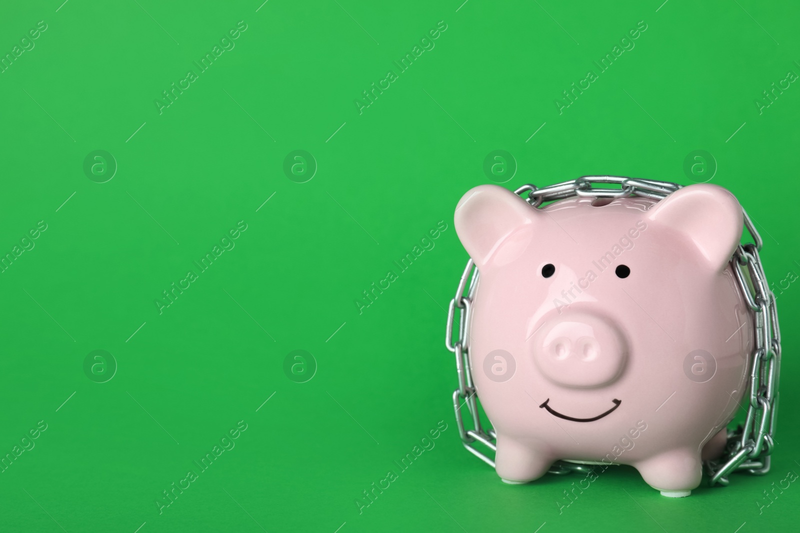 Photo of Piggy bank  with steel chain on green background, space for text. Money safety concept