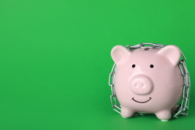 Photo of Piggy bank  with steel chain on green background, space for text. Money safety concept