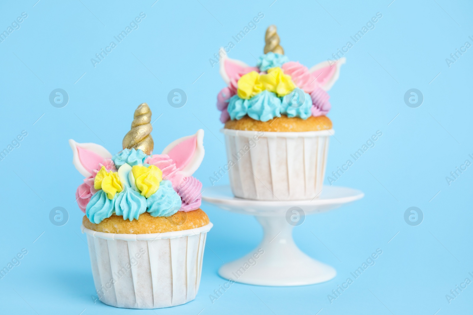 Photo of Cute sweet unicorn cupcakes on light blue background