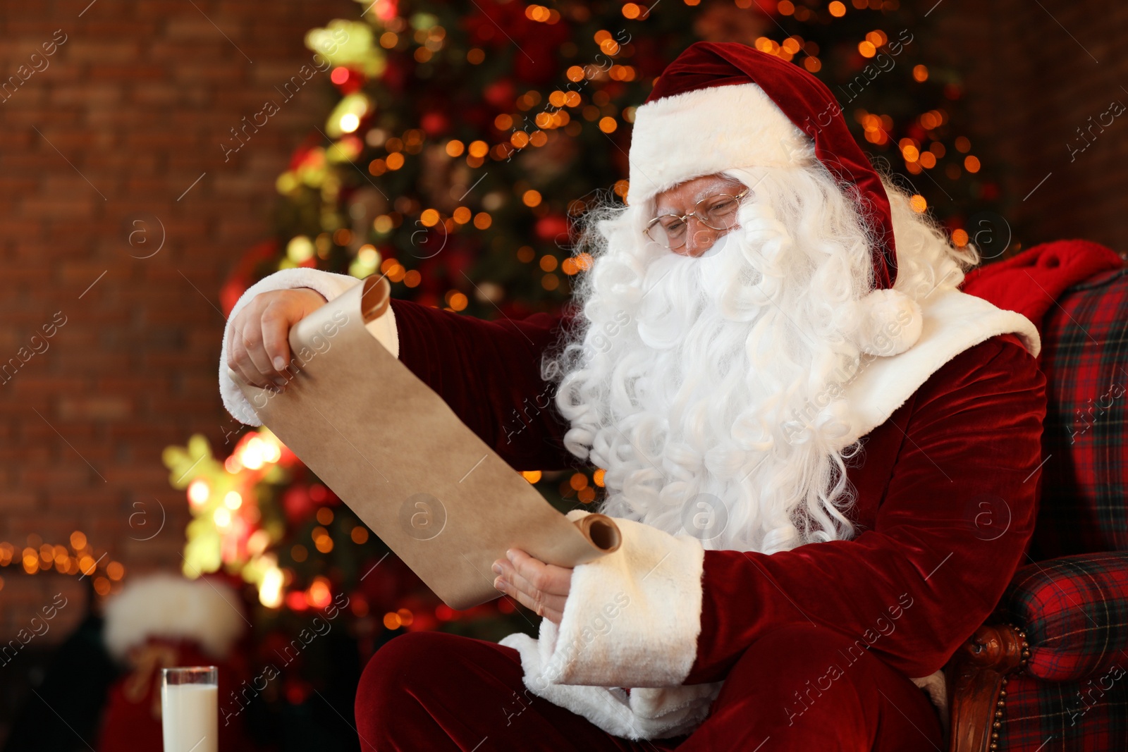 Photo of Santa Claus with wish list near Christmas tree indoors