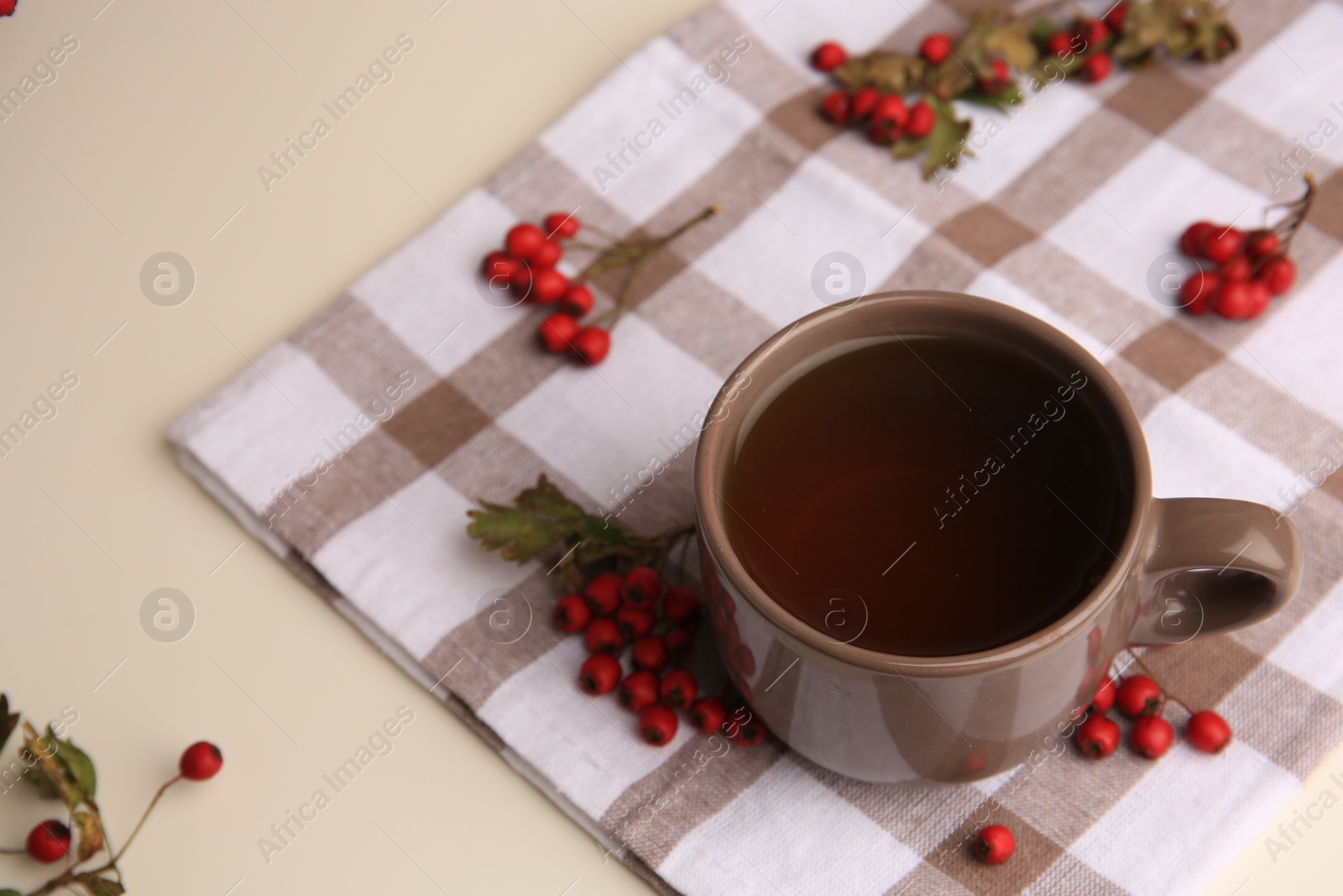 Photo of Brown cup with hawthorn tea and berries on beige table