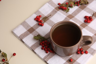 Brown cup with hawthorn tea and berries on beige table