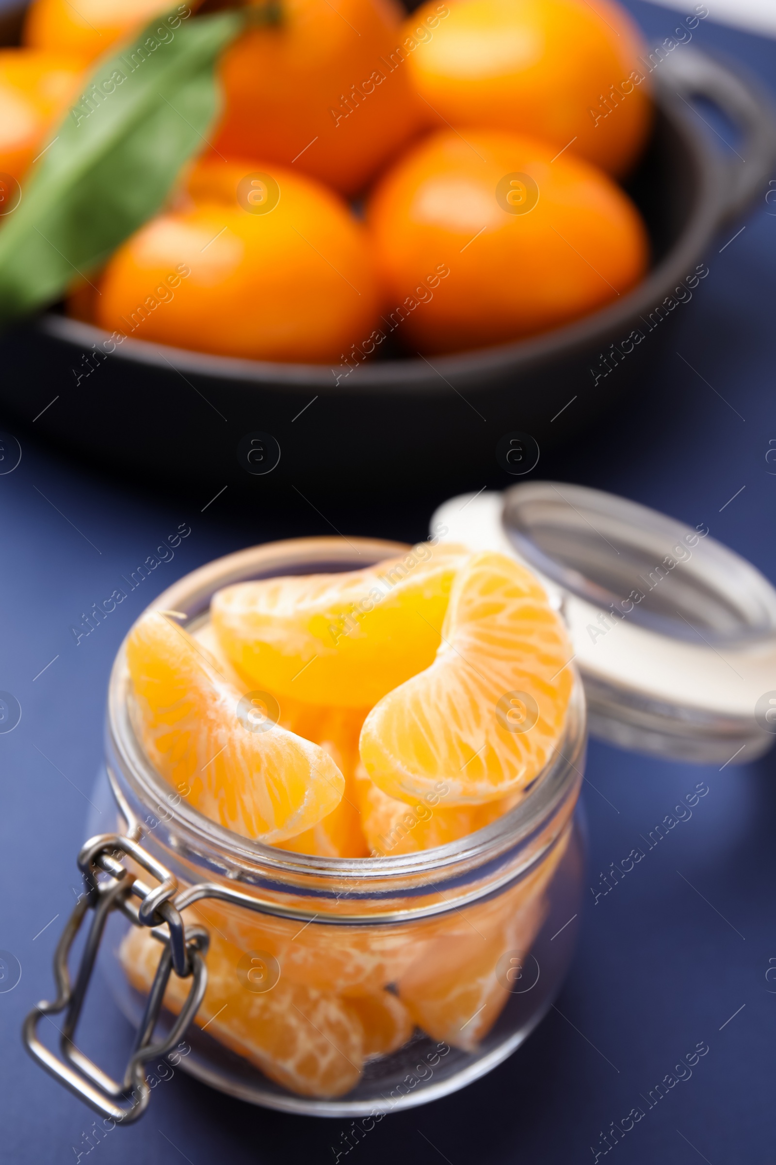 Photo of Glass jar of fresh juicy tangerine segments on blue table, space for text