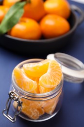 Photo of Glass jar of fresh juicy tangerine segments on blue table, space for text