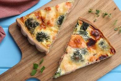 Photo of Pieces of delicious homemade quiche with salmon and broccoli on wooden board, top view