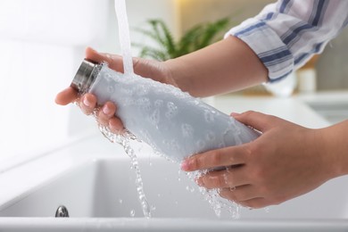 Woman washing thermo bottle in kitchen, closeup