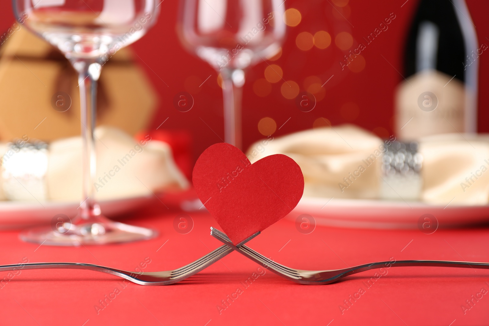 Photo of Joined forks with paper heart on red table, closeup. Romantic dinner