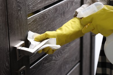 Photo of Woman cleaning door handle with detergent and paper towel, closeup