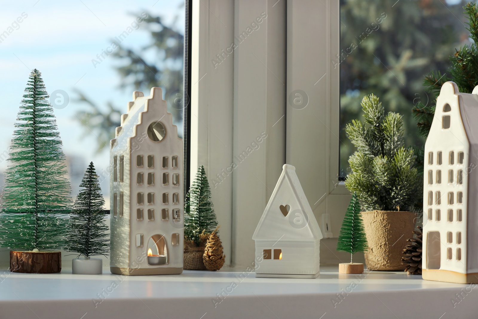 Photo of Beautiful house shaped candle holders and small fir trees on windowsill indoors