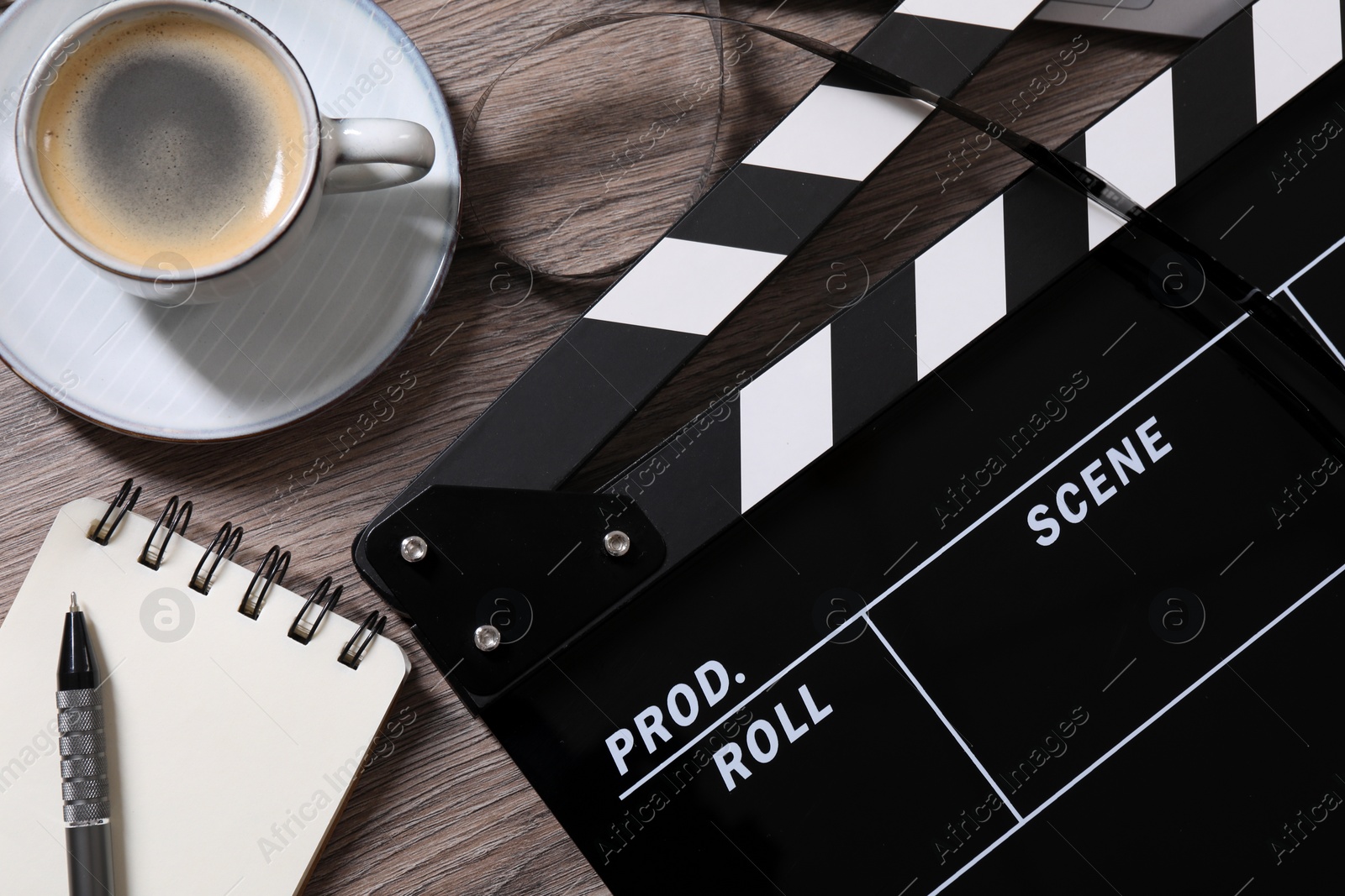 Photo of Movie clapper, film reel, coffee, notebook and pen on wooden table, flat lay