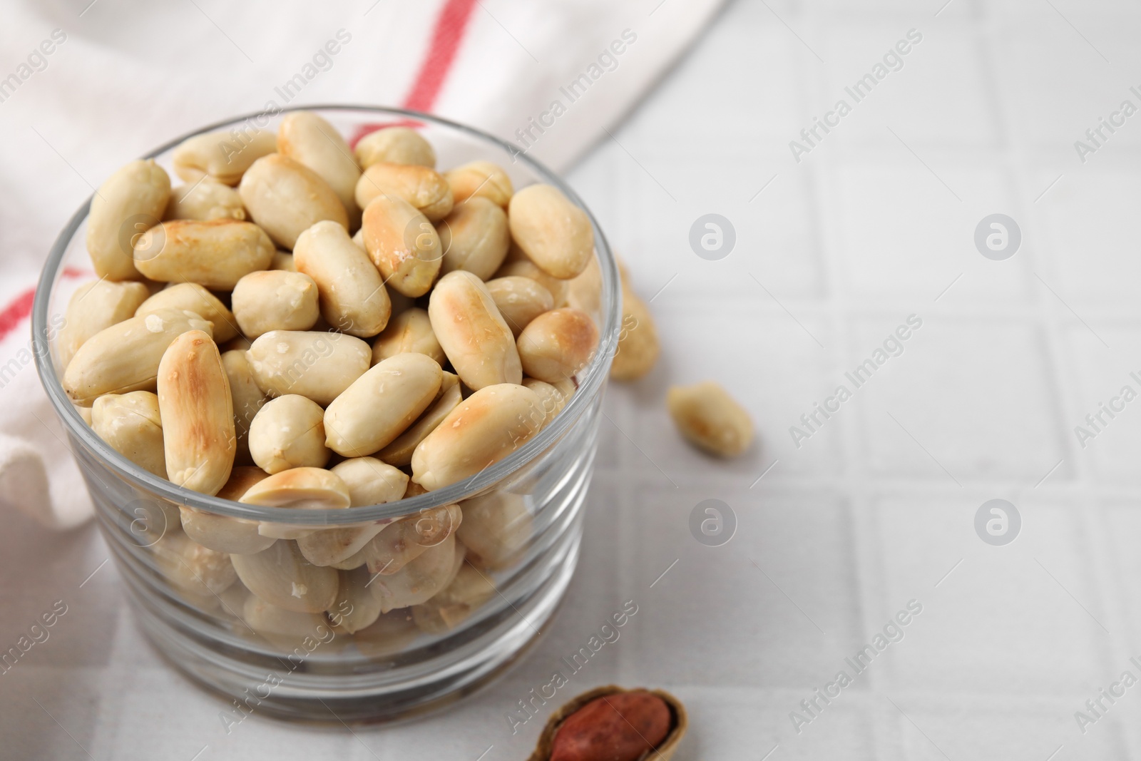 Photo of Roasted peanuts in bowl on white tiled table, closeup. Space for text