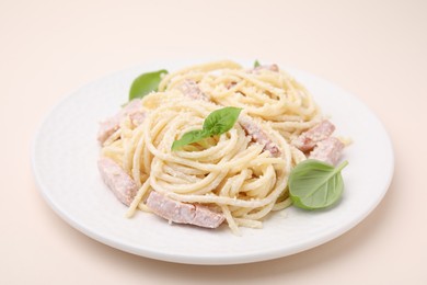 Plate of tasty pasta Carbonara with basil leaves on beige background, closeup