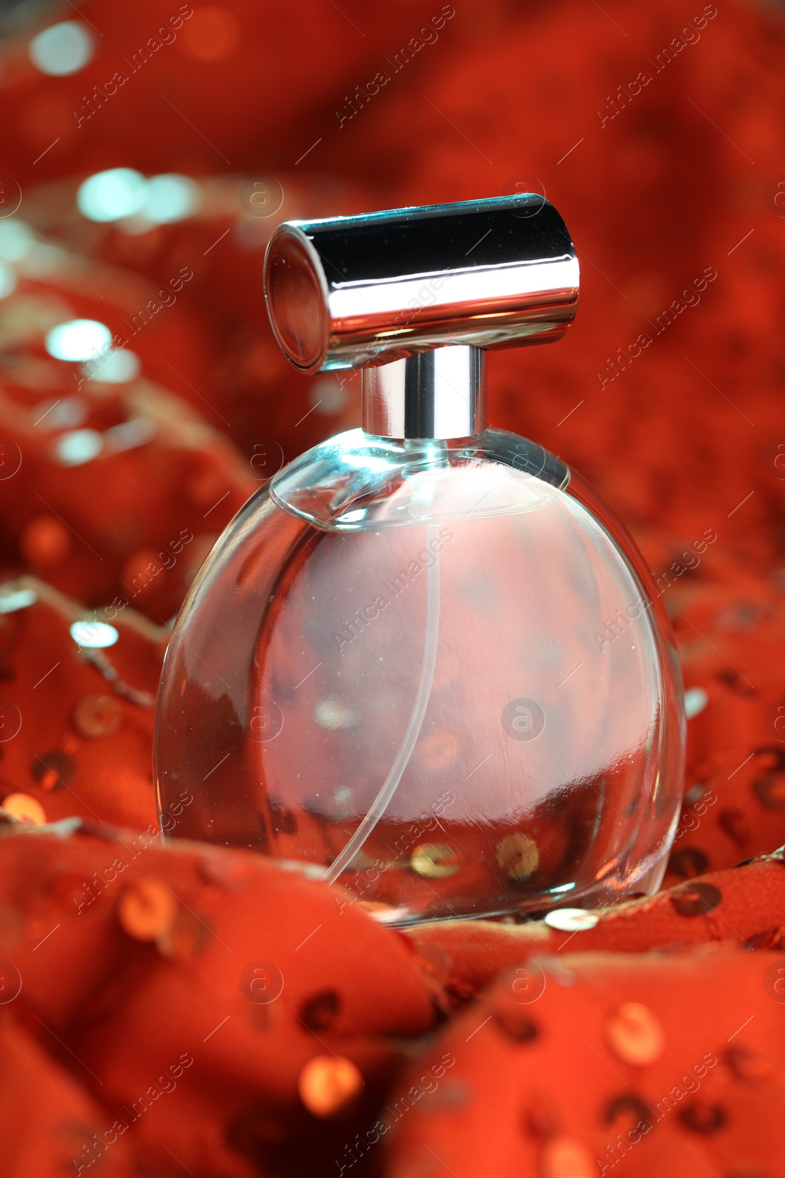 Photo of Luxury perfume in bottle on red fabric with sequins, closeup