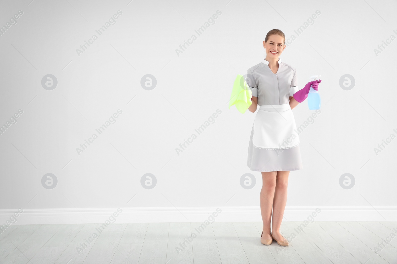 Photo of Young chambermaid with rag and detergent indoors