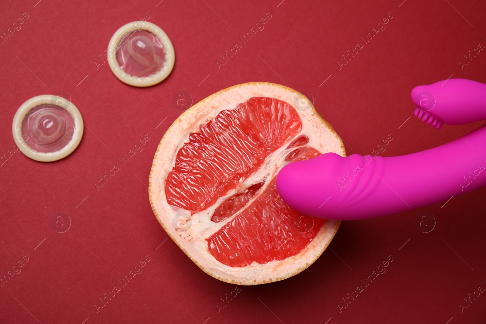 Photo of Half of grapefruit, purple vibrator and condoms on red background, flat lay. Sex concept