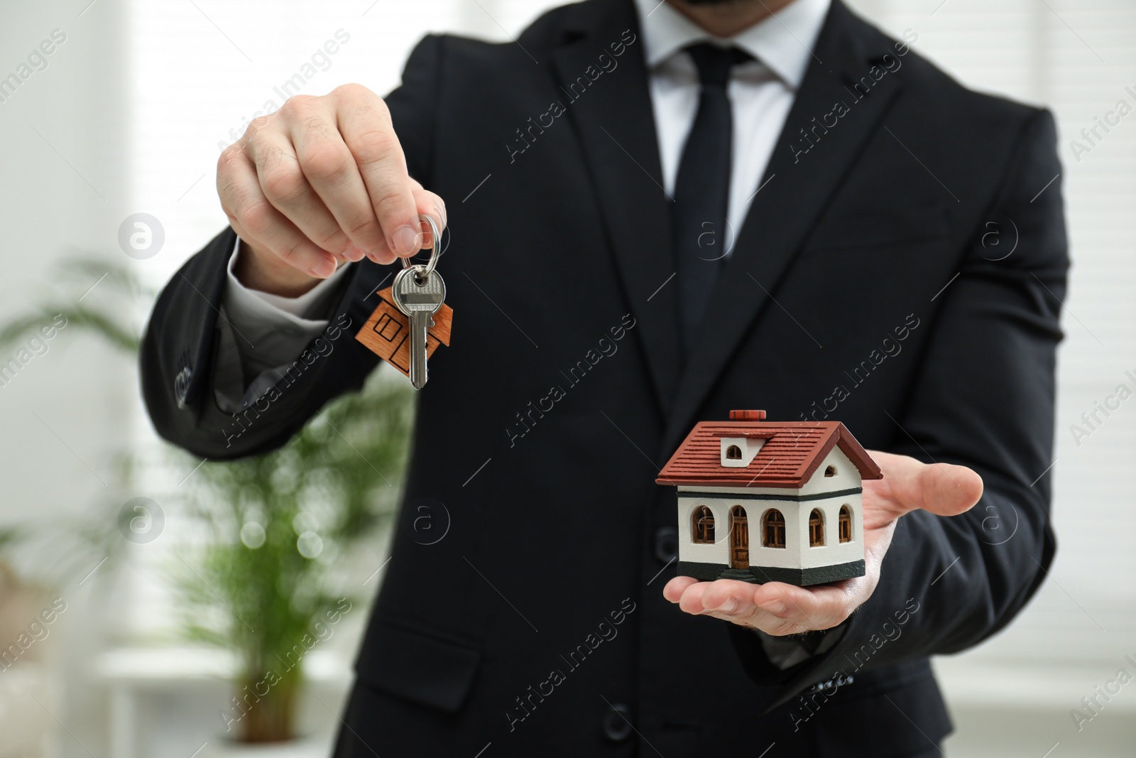 Photo of Real estate agent holding house model and key indoors, closeup