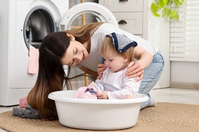 Happy mother with her daughter having fun while washing baby clothes in bathroom