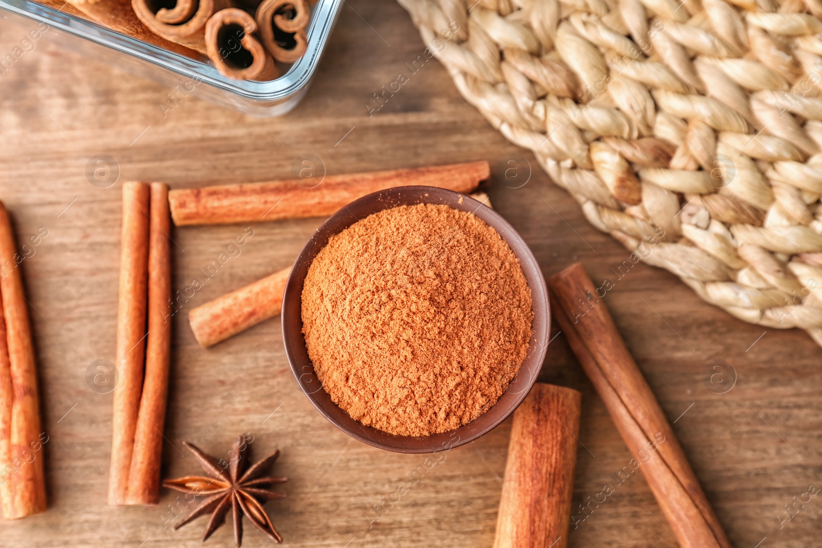 Photo of Bowl with aromatic cinnamon powder and sticks on wooden background