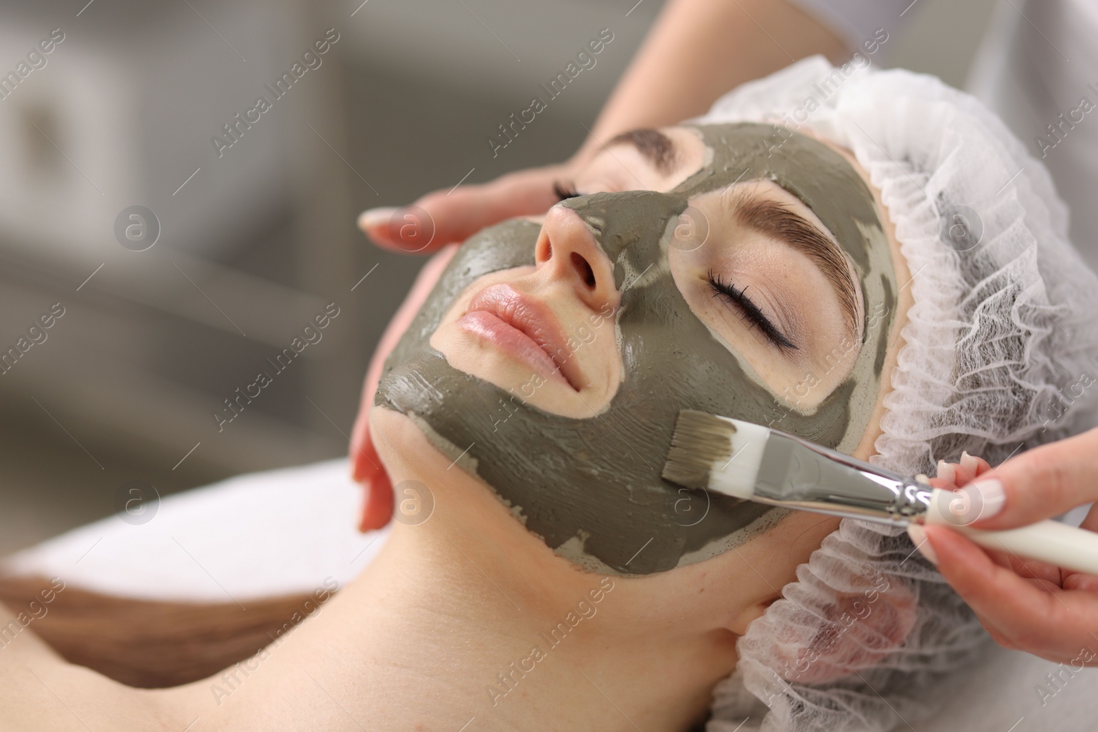 Photo of Cosmetologist applying mask on woman's face in clinic, closeup