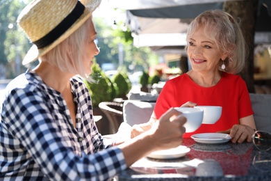 Mature women with cups of coffee talking at table in open air cafe on sunny day
