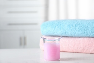 Photo of Laundry detergent in measuring cup near stacked folded towels on table. Space for text