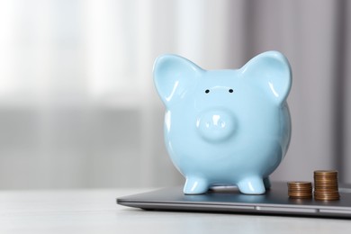 Photo of Piggy bank, stacked coins and laptop on white table indoors. Space for text