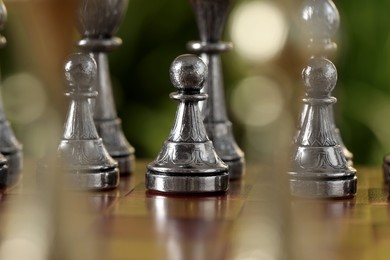 Silver pawns on chess board against blurred background, closeup