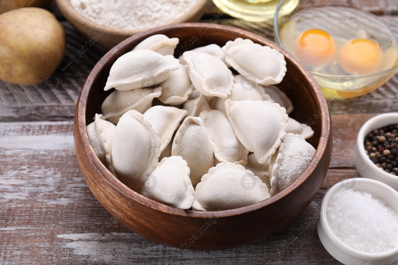 Photo of Raw dumplings (varenyky) and ingredients on wooden table, closeup