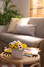 Photo of Cup with beautiful bright flowers and magazines on table in living room, space for text