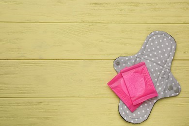 Photo of Disposable and reusable cloth menstrual pads on yellow wooden table, top view. Space for text